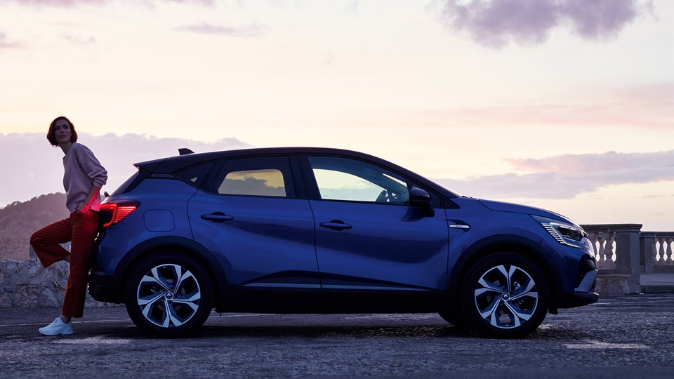 a blue Renault Captur from the side view in a Mountain and a woman is back side of it