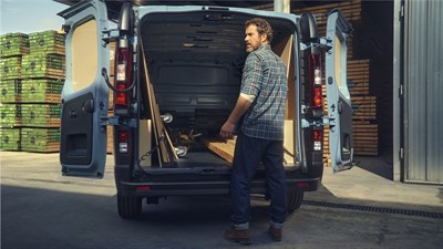 a man at the port backage of the renault new trafic and placing some construction woods inside it